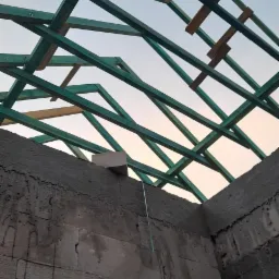 Wznoszenie ścian z bloczków betonowych i konstrukcja drewniana dachu w trakcie budowy domu, widok z dołu na niebo.