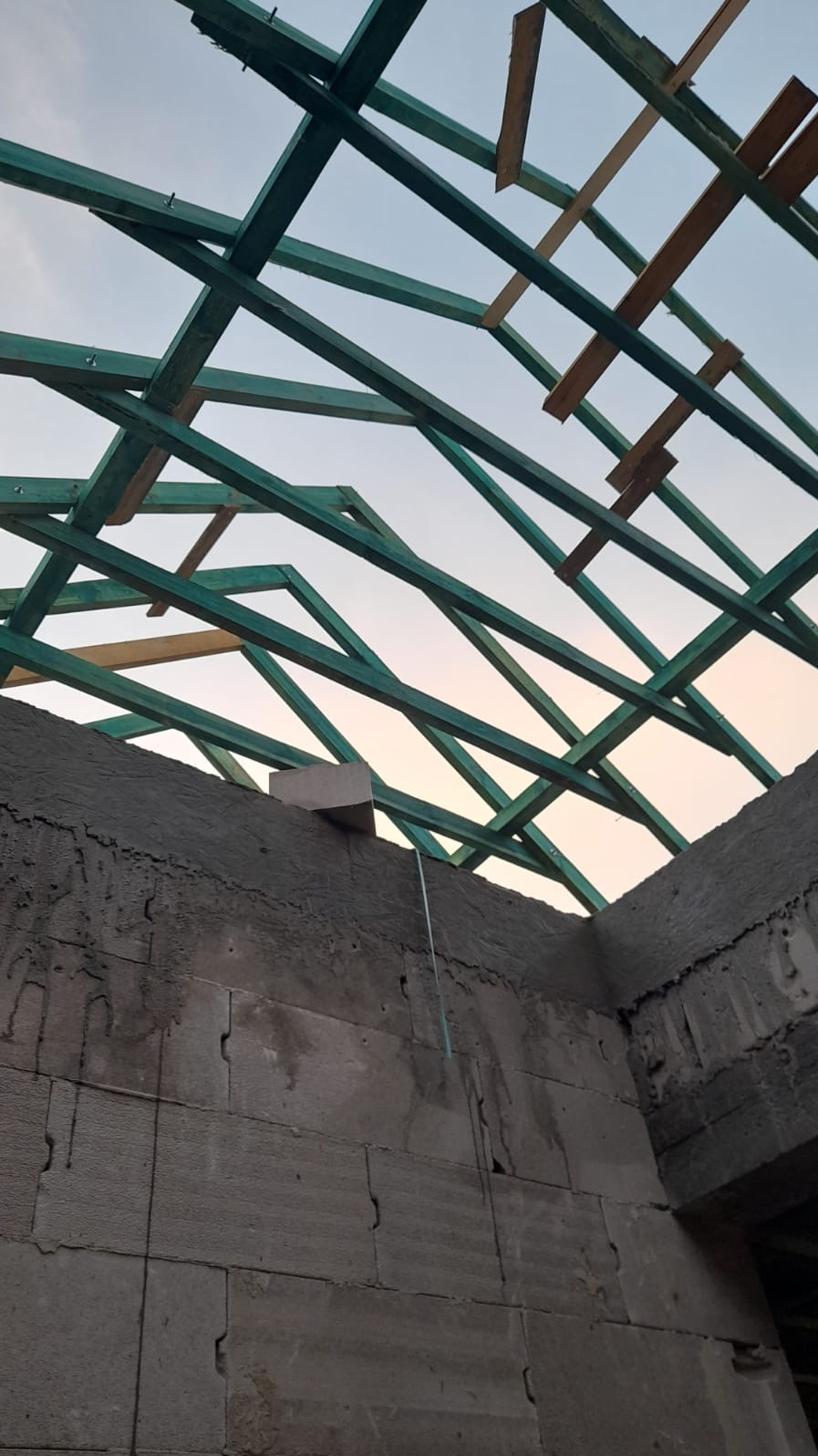 Wznoszenie ścian z bloczków betonowych i konstrukcja drewniana dachu w trakcie budowy domu, widok z dołu na niebo.