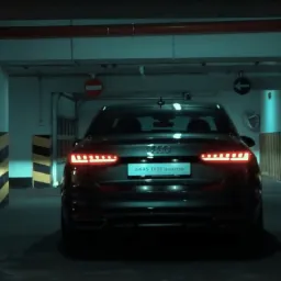 Ciemny samochód Audi A45 TFSI quattro z włączonymi światłami stopu, widziany od tyłu, zaparkowany w garażu podziemnym z kolumnami w żółto-czarne pasy.