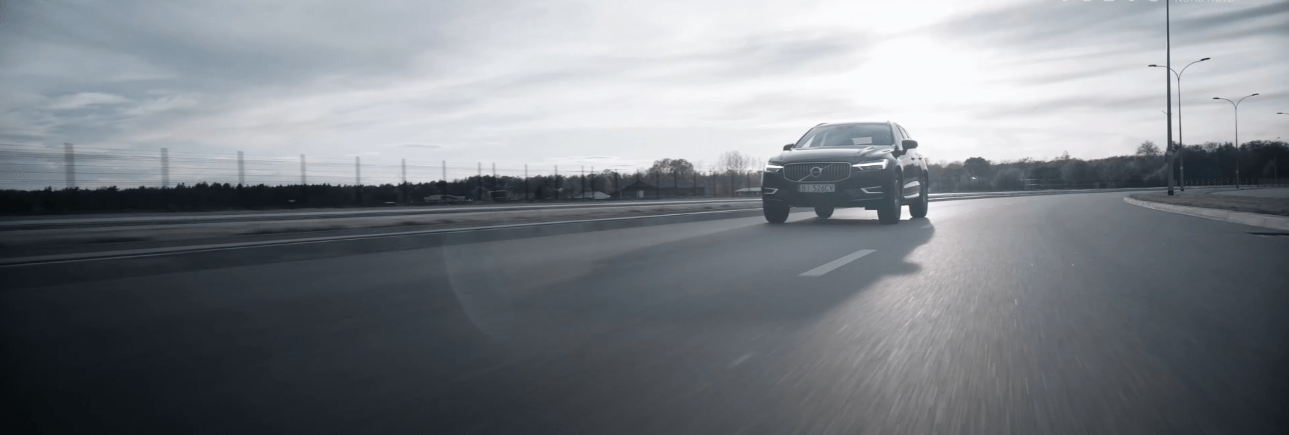 Ciemny SUV Volvo na asfaltowej drodze w słoneczny dzień, widok z niskiej perspektywy, dynamiczne ujęcie w ruchu.