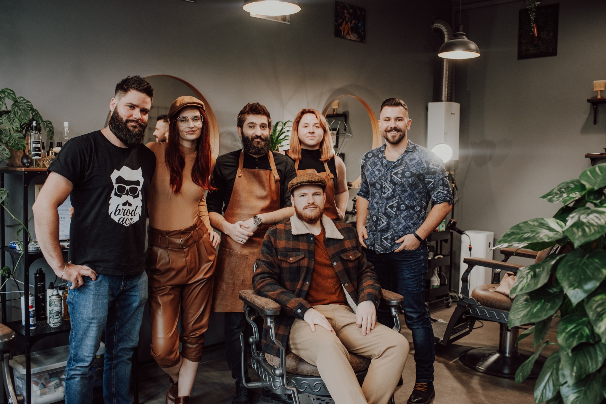Zespół salonu, mężczyzna siedzi w fotelu fryzjerskim, pozostali stoją za nim, w tle lustra i akcesoria