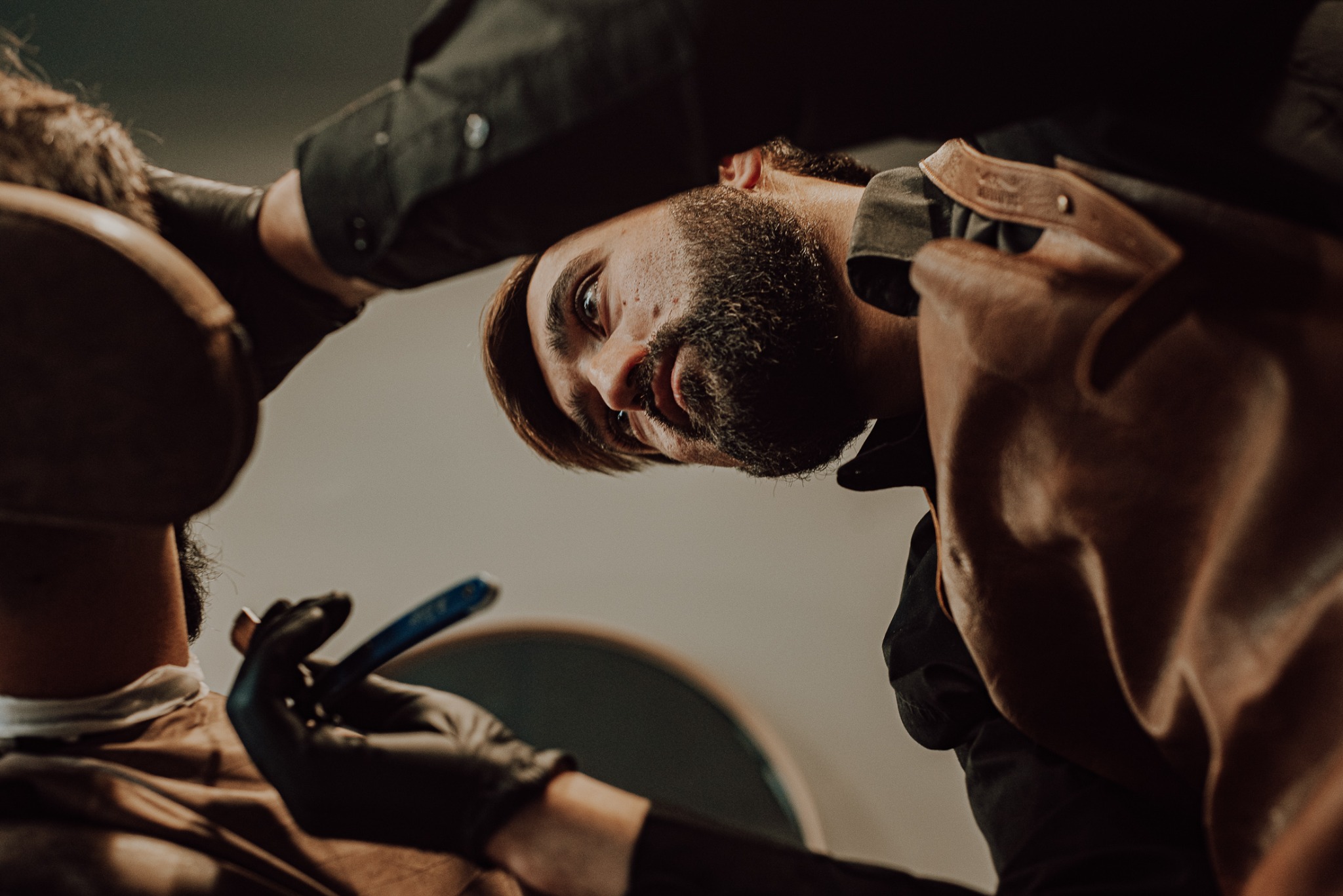 Mężczyzna z brodą podczas golenia brzytwą przez barbera w czarnych rękawiczkach, widok z dołu.