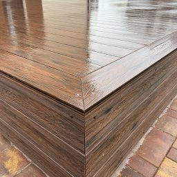 GoldenWood ANGELIKA DOLEGA - Mokry, brązowy taras z desek kompozytowych, z widocznym detalem narożnika i fakturą drewna, po deszczu, na tle kostki brukowej.