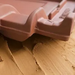 Fragment ceramicznej dachówki zakładkowej w kolorze ceglastym, ułożonej na świeżej zaprawie, widok z bliska.