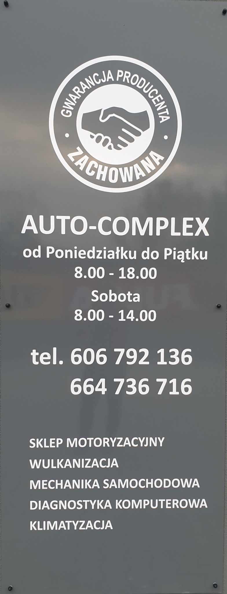 Tablica informacyjna warsztatu samochodowego Auto-Complex z logo 'Gwarancja producenta zachowana', godzinami otwarcia od poniedziałku do soboty oraz numerami telefonów, oferującego usługi takie jak...