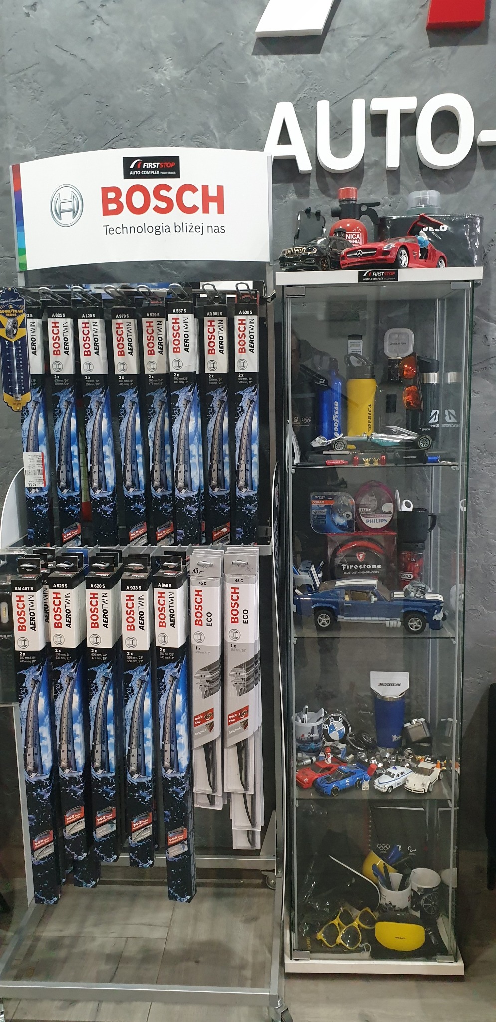 Ekspozycja w sklepie motoryzacyjnym: stojak z opakowaniami wycieraczek Bosch Aerotwin i Bosch Eco, obok gablota z modelami samochodów, akcesoriami motoryzacyjnymi i gadżetami różnych marek...