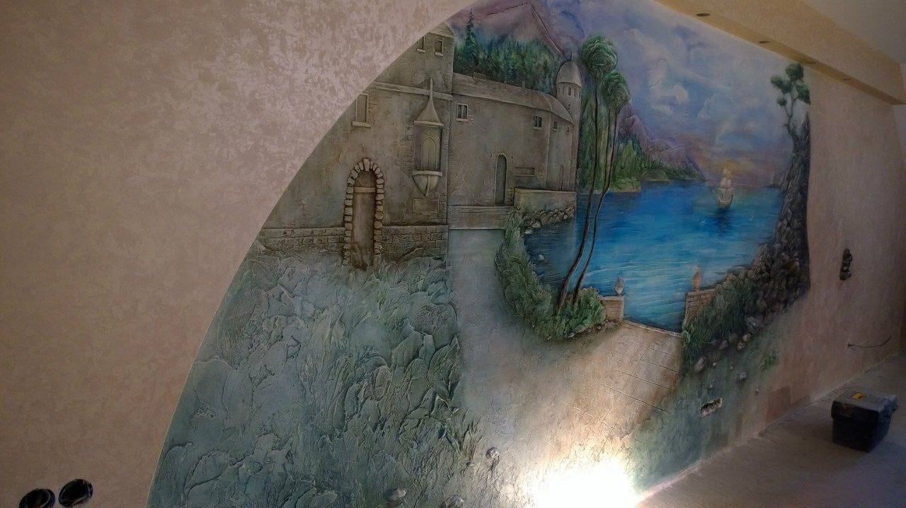 Dekoracyjna ściana w Warszawie z efektem 3D, przedstawiająca pejzaż z zamkiem nad jeziorem i żaglówką. Unikalna faktura i malowanie tworzą iluzję głębi.