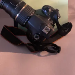 Czarny aparat fotograficzny z obiektywem Tamron leżący na książce o umowach, opisującej stan ich realizacji.