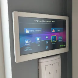 Panel sterowania alarmem Paradox zamontowany na szarej ścianie, z widocznym ekranem dotykowym pokazującym status rozbrojenia i opcje menu.