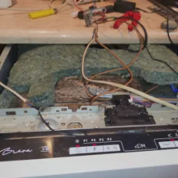 Otwarta zmywarka Brava z widocznymi elementami wewnętrznymi i przewodami, narzędzia na blacie w tle.