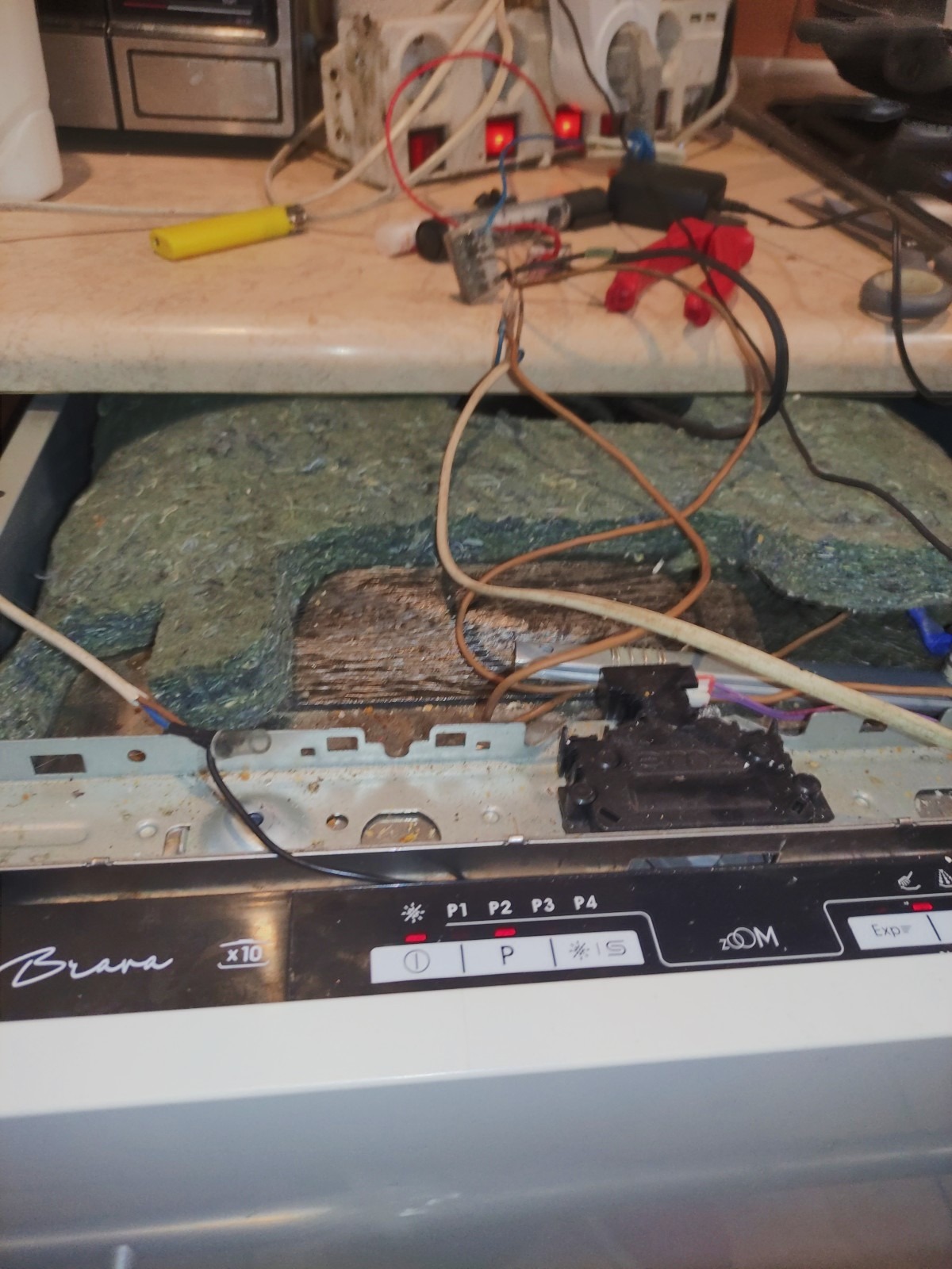 Otwarta zmywarka Brava z widocznymi elementami wewnętrznymi i przewodami, narzędzia na blacie w tle.