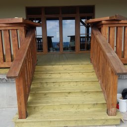 Altany tarasy - Nowe drewniane schody prowadzące na taras, z brązowymi balustradami, pomalowane na jasnozielony kolor, widok z dołu.