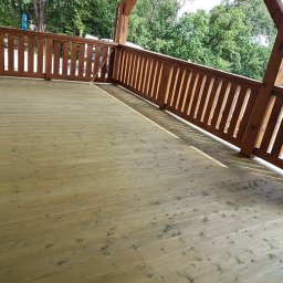 Altany tarasy - Świeżo wykończony taras z jasnego drewna z brązową balustradą, widok na zieleń w tle.