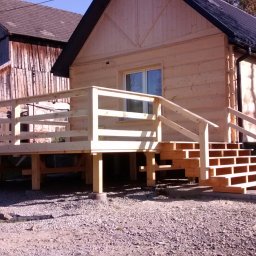 Altany tarasy - Surowy drewniany dom z nowo wybudowanym tarasem i schodami, widoczne ślady prac budowlanych na gruncie.