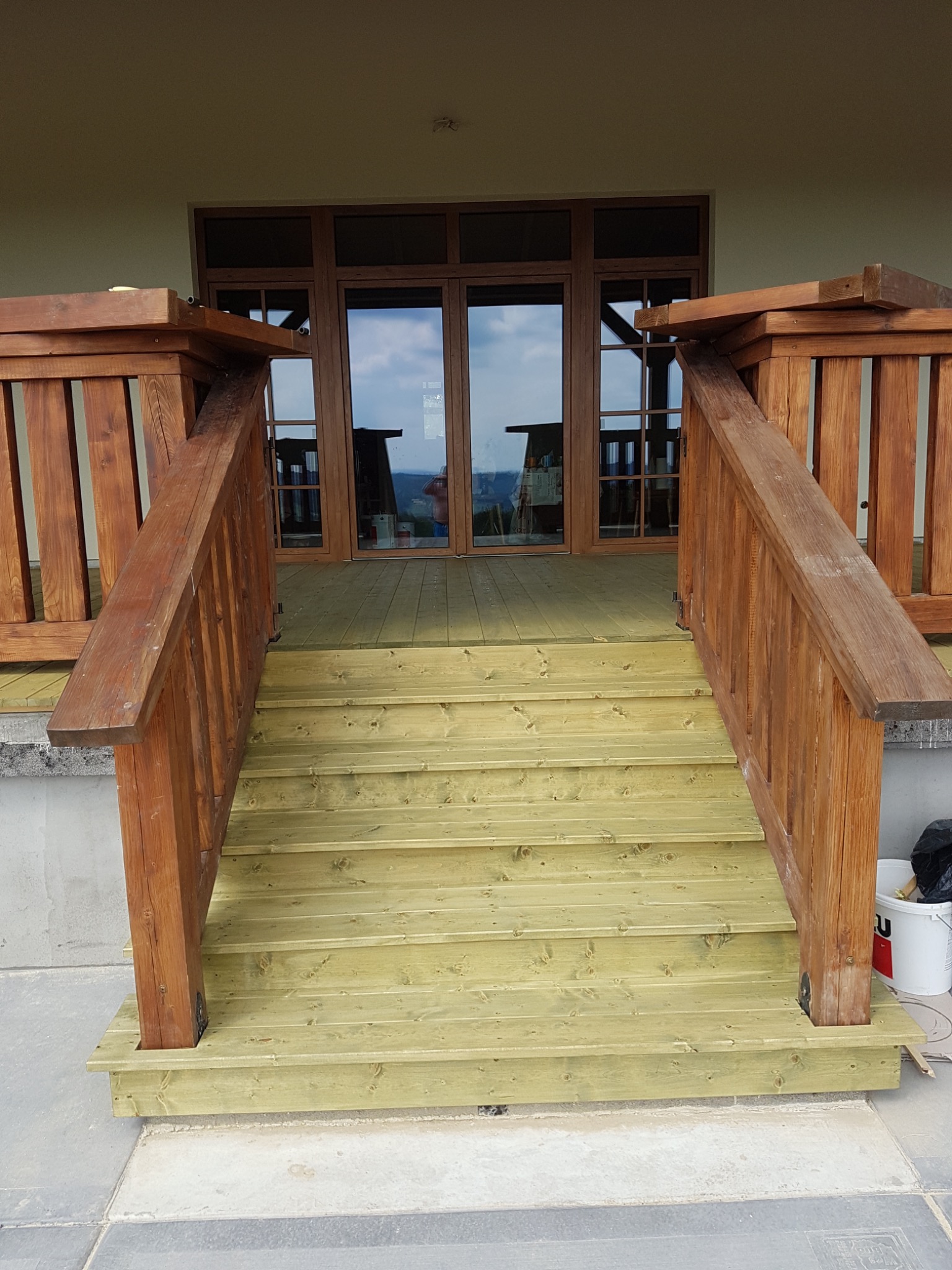 Nowe drewniane schody prowadzące na taras, z brązowymi balustradami, pomalowane na jasnozielony kolor, widok z dołu.