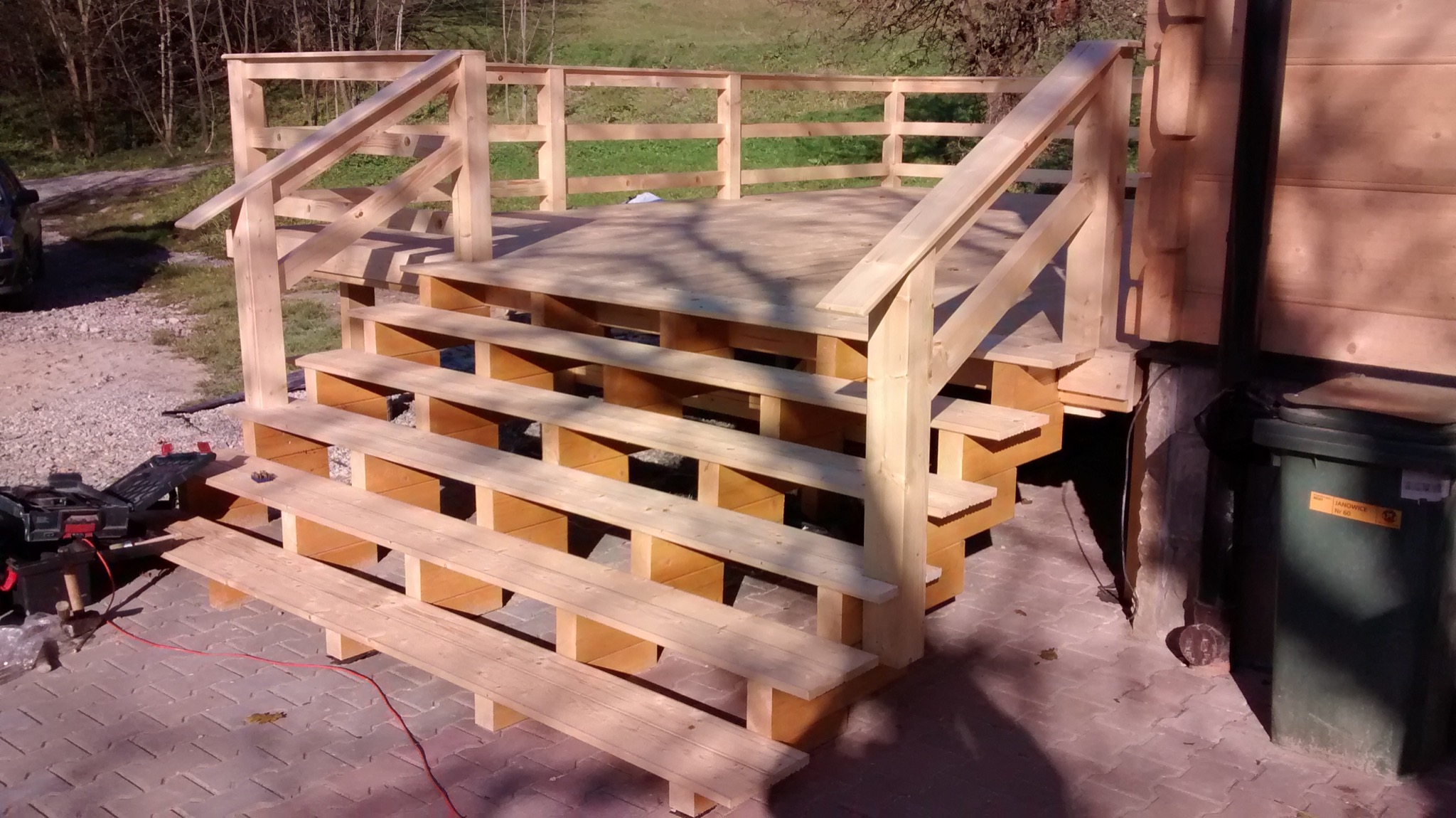 Surowe drewniane schody prowadzące na podest, widoczne narzędzia i kabel zasilający, wskazujące na trwające prace wykończeniowe.