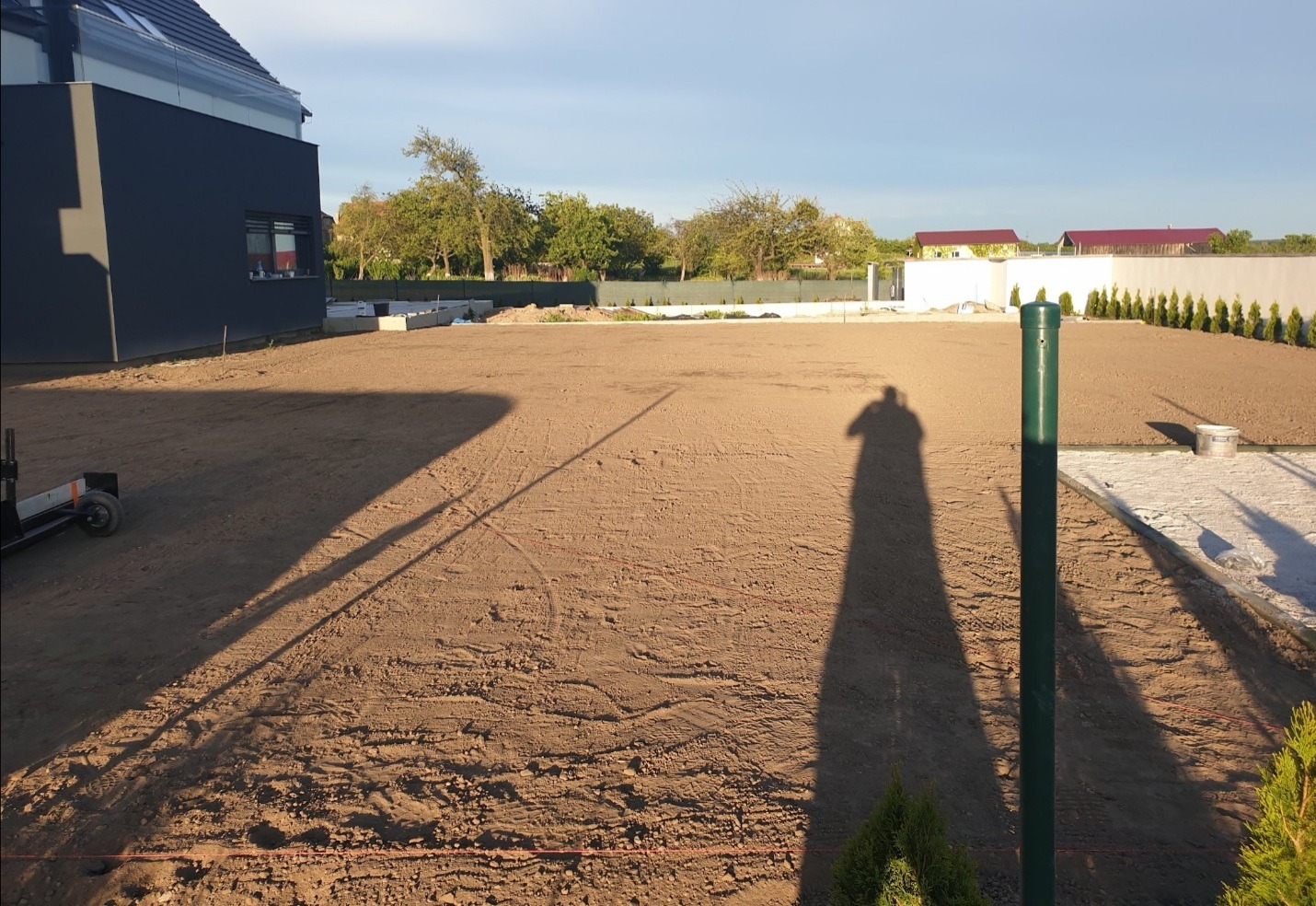 Przygotowany teren pod budowę z widocznym śladem po maszynie, wytyczonymi granicami i cieniem osoby fotografującej.