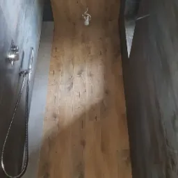 Nowoczesna kabina prysznicowa z deszczownicą i panelami imitującymi drewno, oświetlona przez żarówkę na kablu