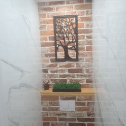 Part Home - Wnętrze łazienki z toaletą wiszącą, obudowaną cegłą klinkierową, dekoracją ścienną w kształcie drzewa, półką z mchem i marmurowymi płytkami na ścianach.