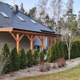 Part Home - Nowoczesny dom jednorodzinny z ciemną dachówką i drewnianą pergolą, widok na zadbany trawnik i rząd tuj w słoneczny dzień.