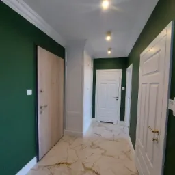 Korytarz po remoncie z ciemnozielonymi ścianami, marmurową podłogą, białymi drzwiami i zabudowaną szafą wnękową.