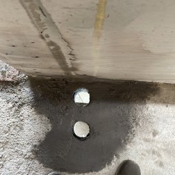 MOJO Damian Mojecki - Dwa wywiercone otwory w ścianie, zalane szarą masą, widok z góry na stopy w butach roboczych. Prace hydrauliczne w Kielcach.