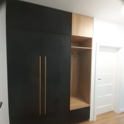 INSIDE Anna Weyna - Czarno-drewniana szafa wnękowa z otwartą półką i złotymi uchwytami, widok z boku na tle białej ściany i drzwi.