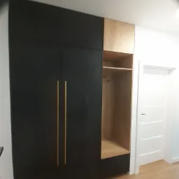 Czarno-drewniana szafa wnękowa z otwartą półką i złotymi uchwytami, widok z boku na tle białej ściany i drzwi.