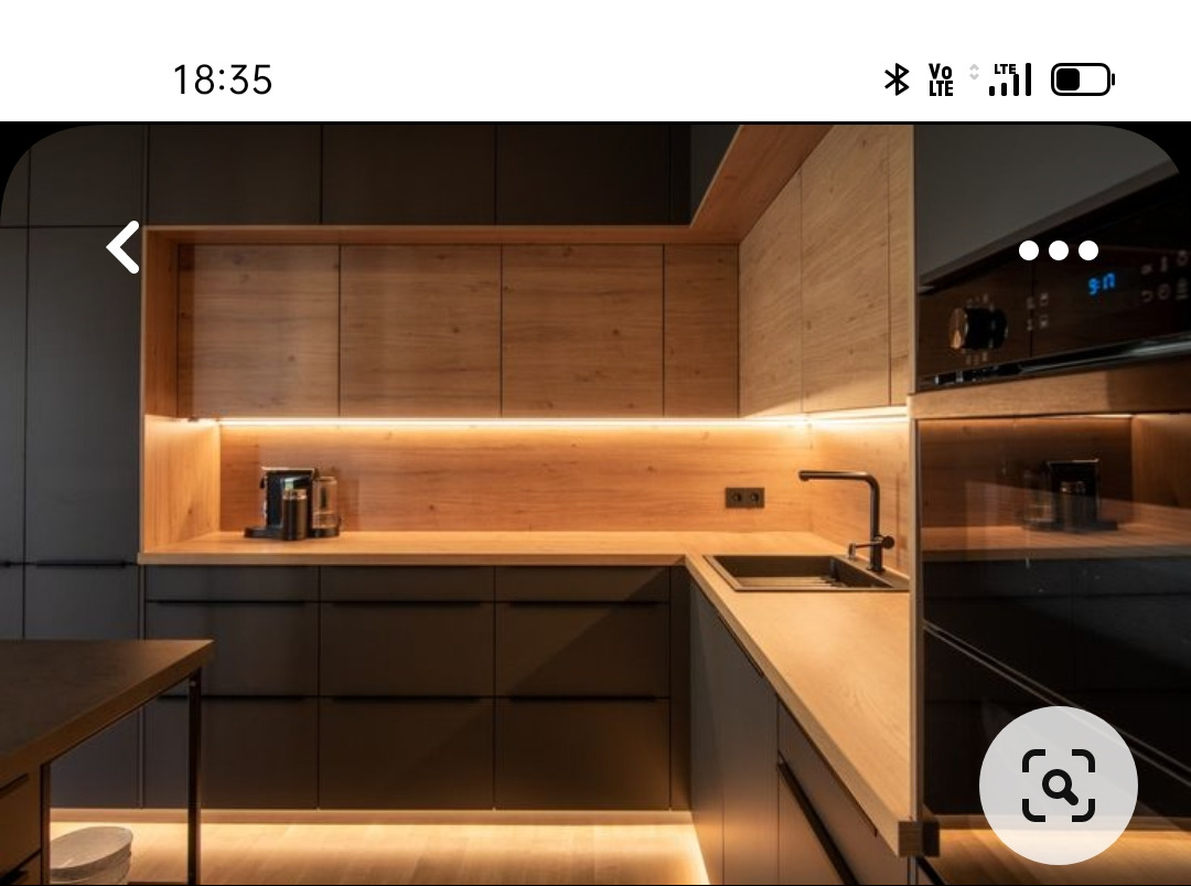 Nowoczesna kuchnia: czarne, matowe fronty szafek dolnych, drewniane szafki górne z podświetleniem LED, czarny zlew i bateria, sprzęt AGD w zabudowie.