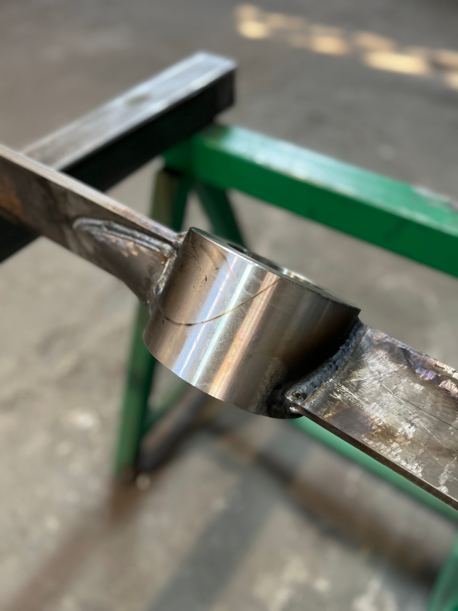 Szlifowany element metalowy z widocznymi spawami na tle warsztatowym.