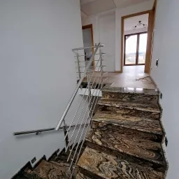 Schody z egzotycznego kamienia z błyszczącą, metalową barierką i poręczą w nowoczesnym domu.