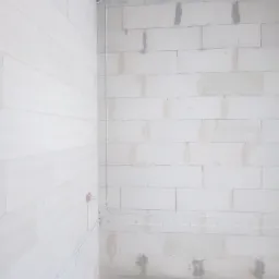 Wnętrze w trakcie prac instalacyjnych: białe ściany z betonu komórkowego, pionowo poprowadzone kable elektryczne przytwierdzone klamrami, widoczne puszki instalacyjne w ścianie.