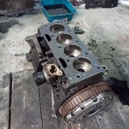 Silnik 1.9 dci w trakcie naprawy w Zabrzu, widoczna głowica cylindrów z uszczelką, filtr oleju i koło zamachowe. Tło warsztatowe, niebieska miska na części.