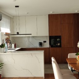 Krzysztof Rozum - Nowoczesna kuchnia z białymi i drewnianymi szafkami, blatem z białego marmuru i drewnianą podłogą, oświetlona światłem słonecznym.