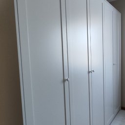 Krzysztof Rozum - Biała szafa wnękowa z czterema drzwiami, z okrągłymi uchwytami, zamontowana od podłogi do sufitu w jasnym pomieszczeniu.