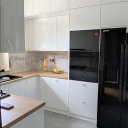 Krzysztof Rozum - Jasna kuchnia z białymi szafkami i drewnianym blatem, widoczna podczas remontu, ściana częściowo bez wykończenia, na blacie owoce i napoje.