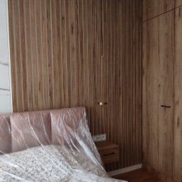 Krzysztof Rozum - Sypialnia z drewnianą boazerią ścienną, szafą w zabudowie i łóżkiem przykrytym folią ochronną.