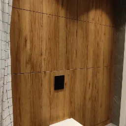 Nowoczesna łazienka z zabudową z drewnopodobnych paneli, wiszącą toaletą i szarą marmurową podłogą.