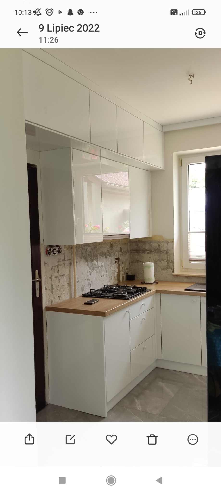 Wnętrze kuchni w trakcie remontu: białe, lakierowane szafki wiszące i dolne z drewnianym blatem, widoczne ślady po starych płytkach na ścianie, płyta gazowa na blacie.