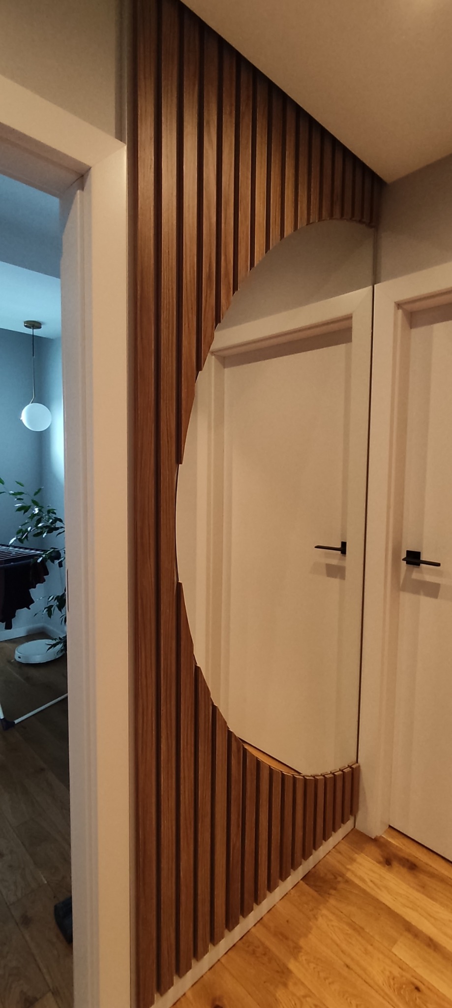 Nowoczesna aranżacja przedpokoju z lustrem wkomponowanym w drewniane lamele, przylegające do białych drzwi.