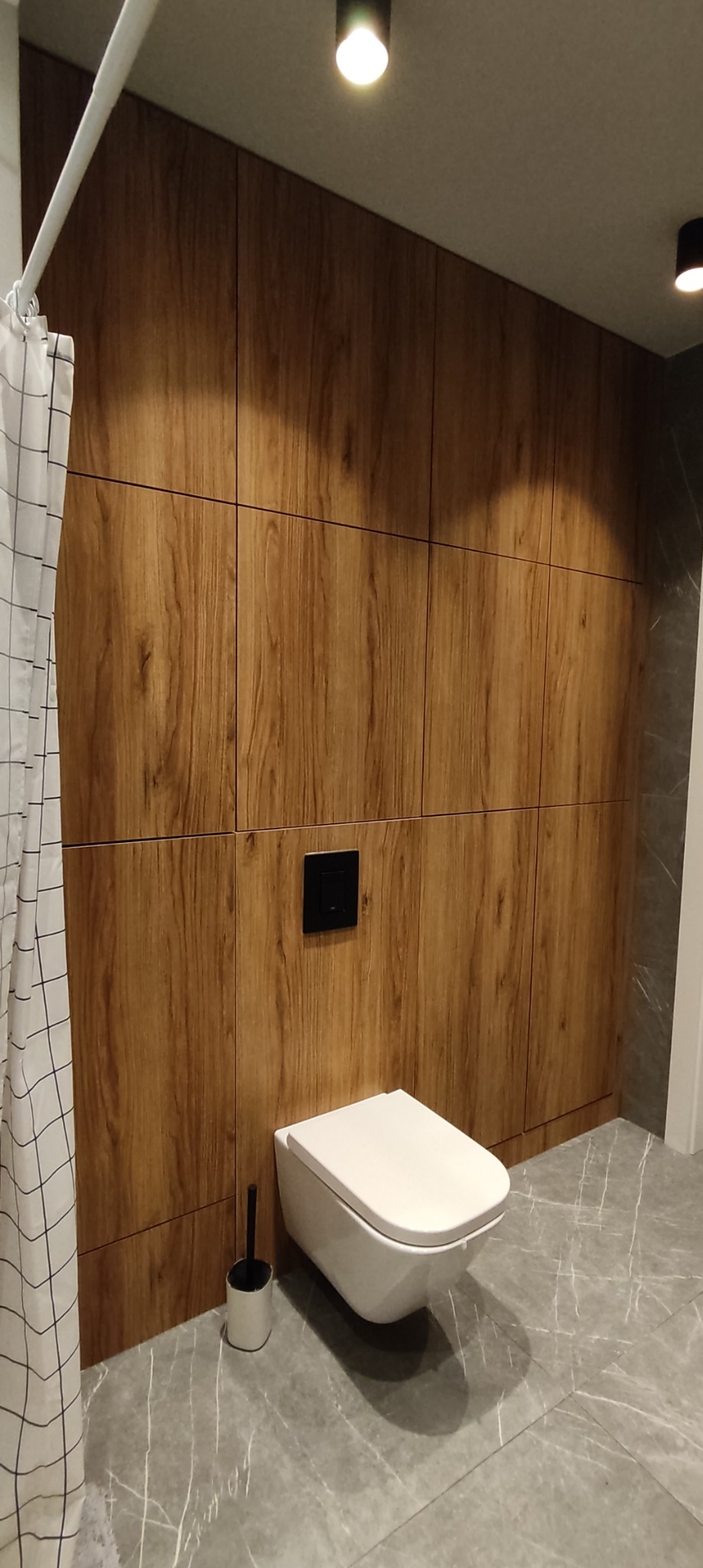 Nowoczesna łazienka z zabudową z drewnopodobnych paneli, wiszącą toaletą i szarą marmurową podłogą.