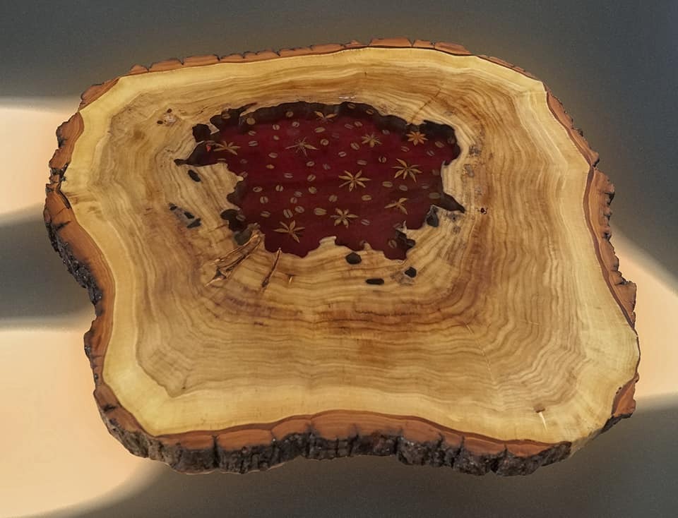 Przekrój pnia drzewa z żywicą epoksydową w kolorze czerwonym, wypełnioną ziarnami kawy i anyżem gwiaździstym, widoczne słoje drzewa.