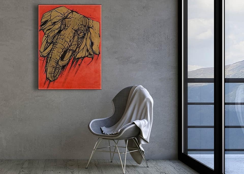 Wnętrze pokoju z szarą ścianą, na której wisi obraz z motywem słonia na pomarańczowym tle, obok okna z widokiem na góry oraz krzesła przykrytego białym kocem.