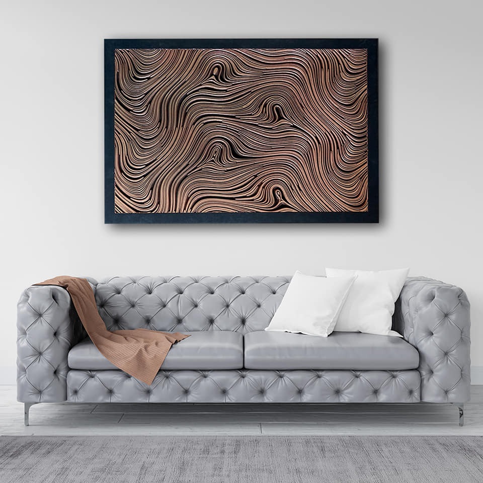 Szary skórzany chesterfield z brązowym pledem i białymi poduszkami na tle ściany z abstrakcyjnym obrazem w czarnej ramie.