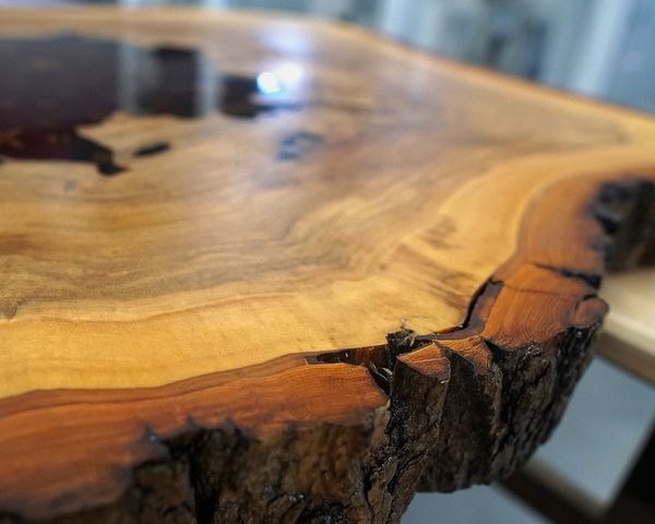 Blat stołu z litego drewna z żywicą epoksydową, widoczne słoje i kora na krawędzi, wykończony na wysoki połysk.