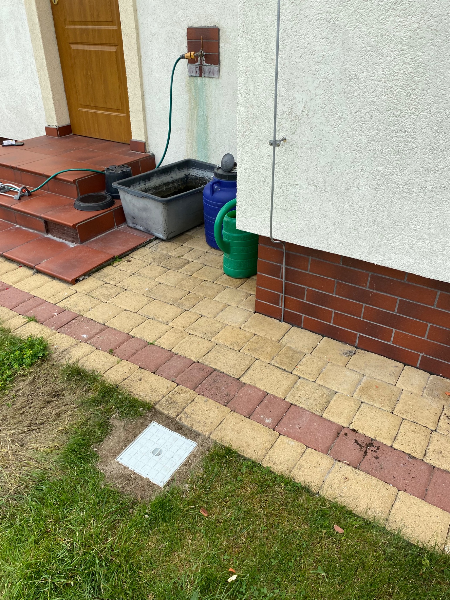 Instalacja wodna z kranem na zewnątrz domu w Koninie, z widocznymi śladami po przeciekach i podłączonym wężem ogrodowym, prowadzącym do zbiornika na wodę.