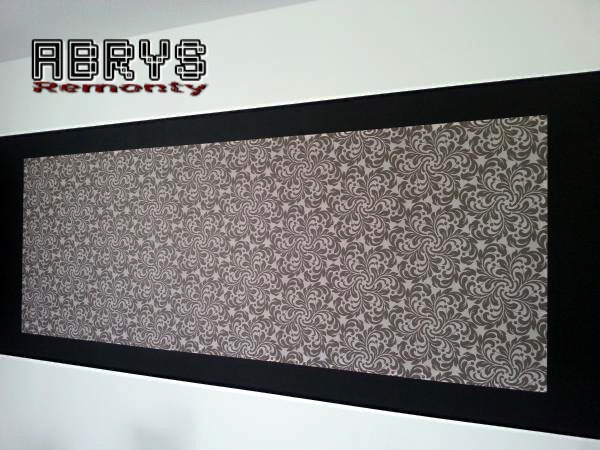 Prostokątna dekoracja ścienna z wzorzystą tapetą w odcieniach szarości, otoczona czarną ramą na białej ścianie, z widocznym logo firmy w górnym lewym rogu.