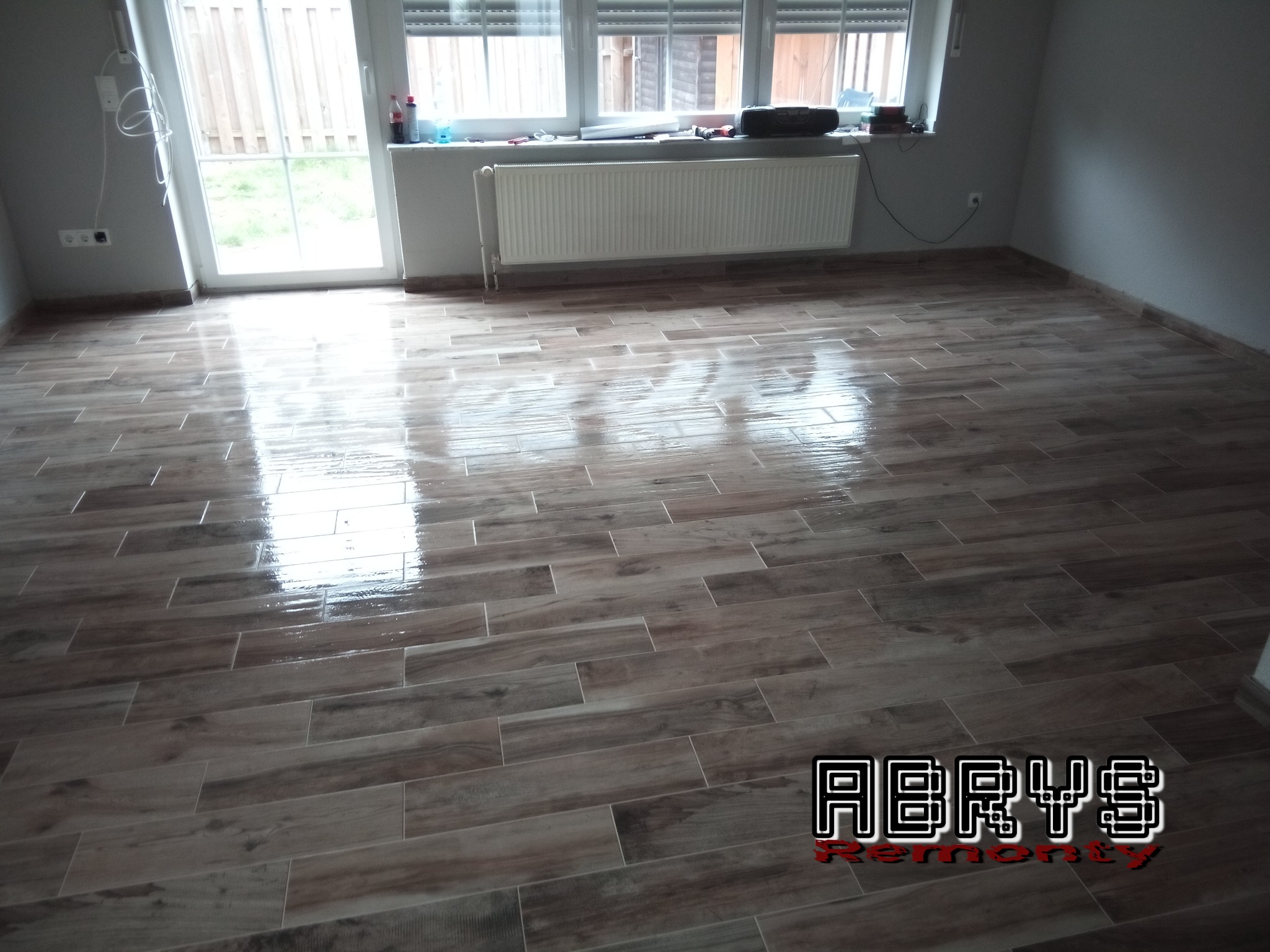 Ułożona podłoga z płytek imitujących drewno w jasnym wnętrzu w Sadlnie, widoczny fragment okna i grzejnika, podłoga świeżo po umyciu.