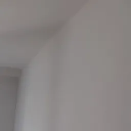 Świeżo pomalowany róg pokoju z widocznym łączeniem ściany i sufitu, wykończony na gładko, w jasnym odcieniu bieli.