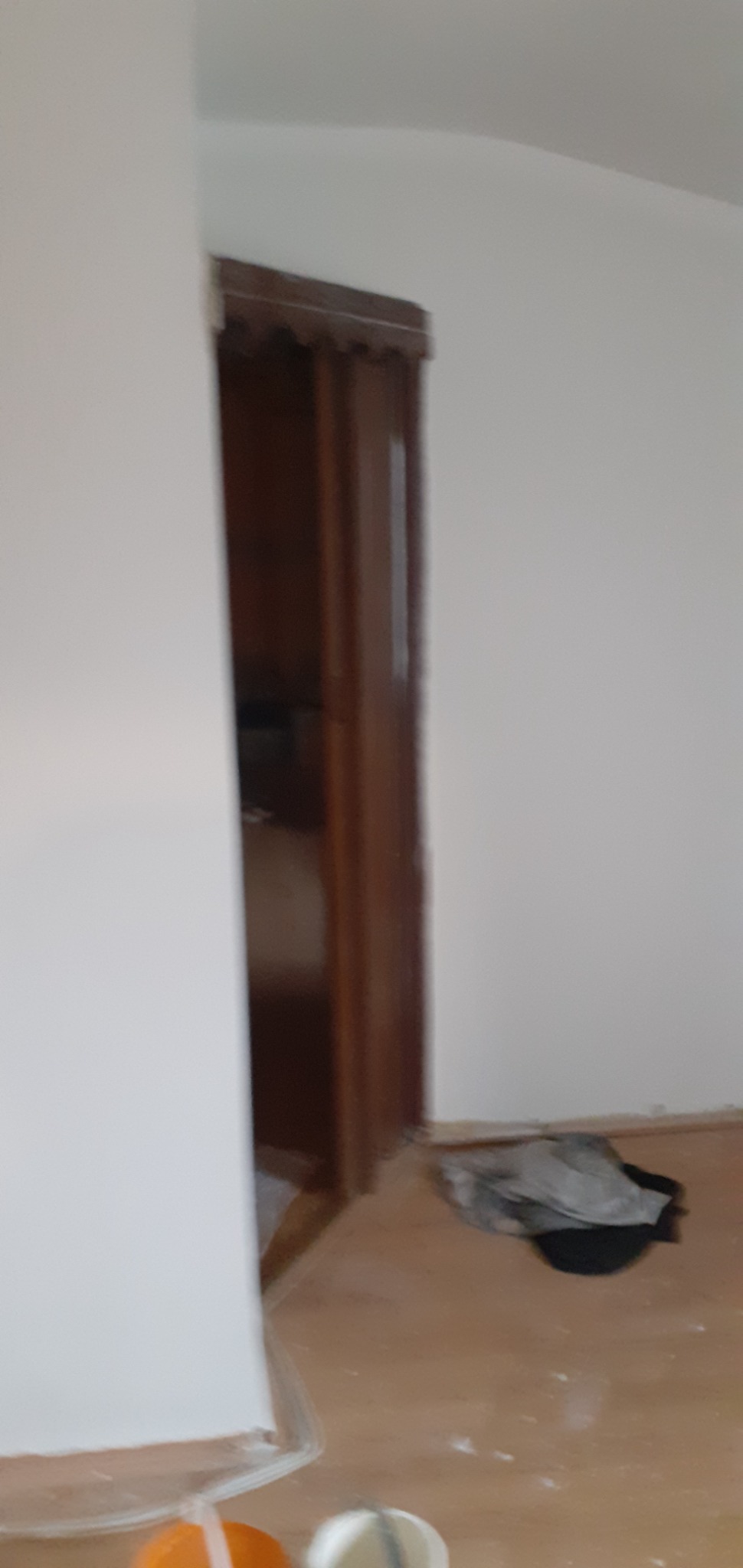 Świeżo pomalowane na biało ściany z brązową futryną drzwiową. Na podłodze widoczne ślady po remoncie, przy ścianie leżące materiały budowlane.